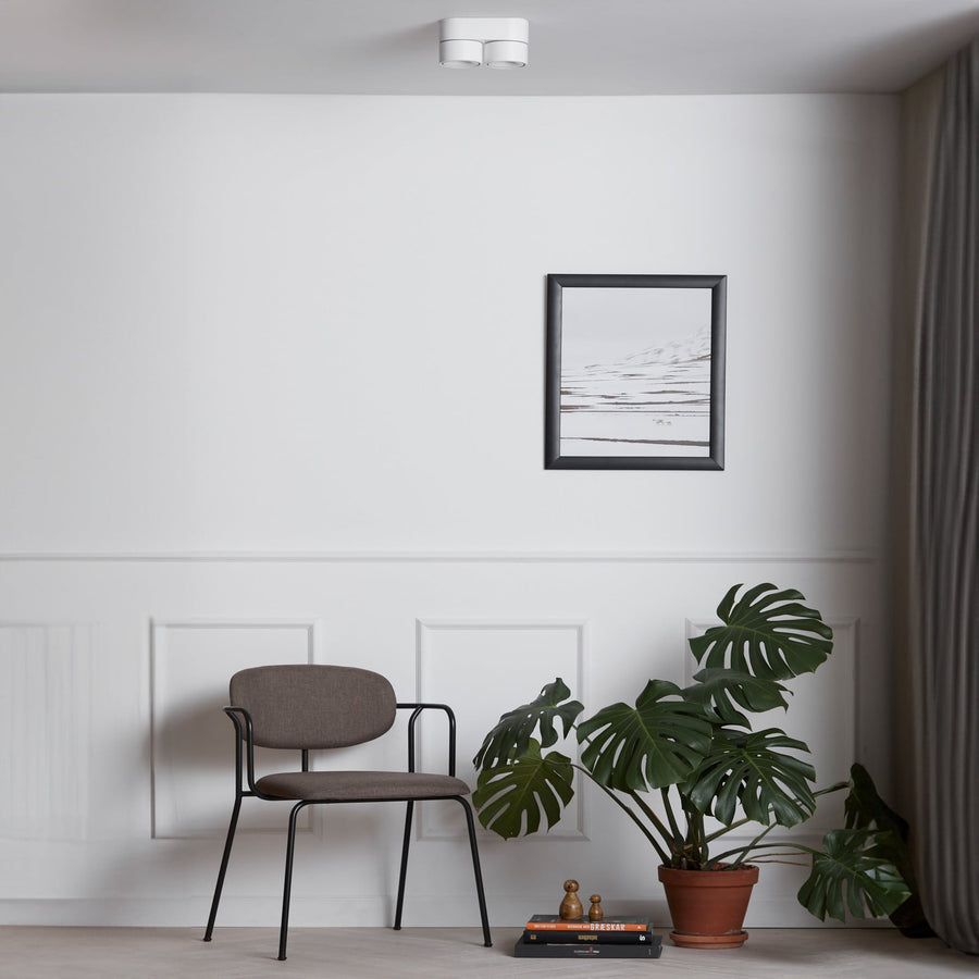 Luminaire blanc fixé au plafond dans un salon minimaliste, avec chaise et plante.