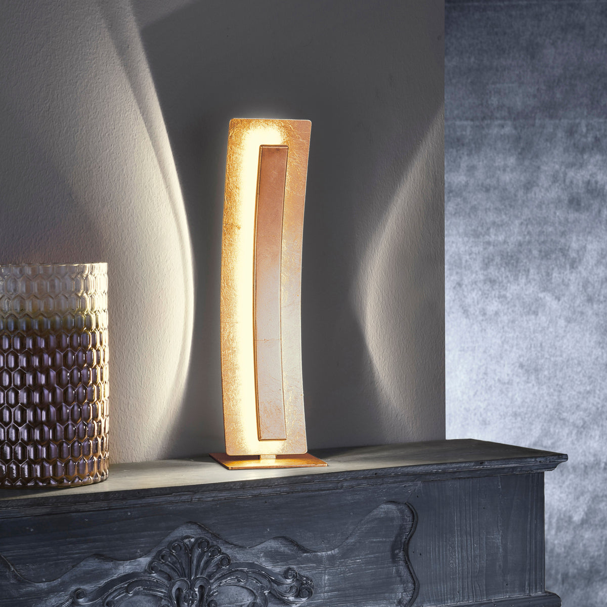 Mise en ambiance de la lampe dorée sur une cheminée sombre, éclairage indirect