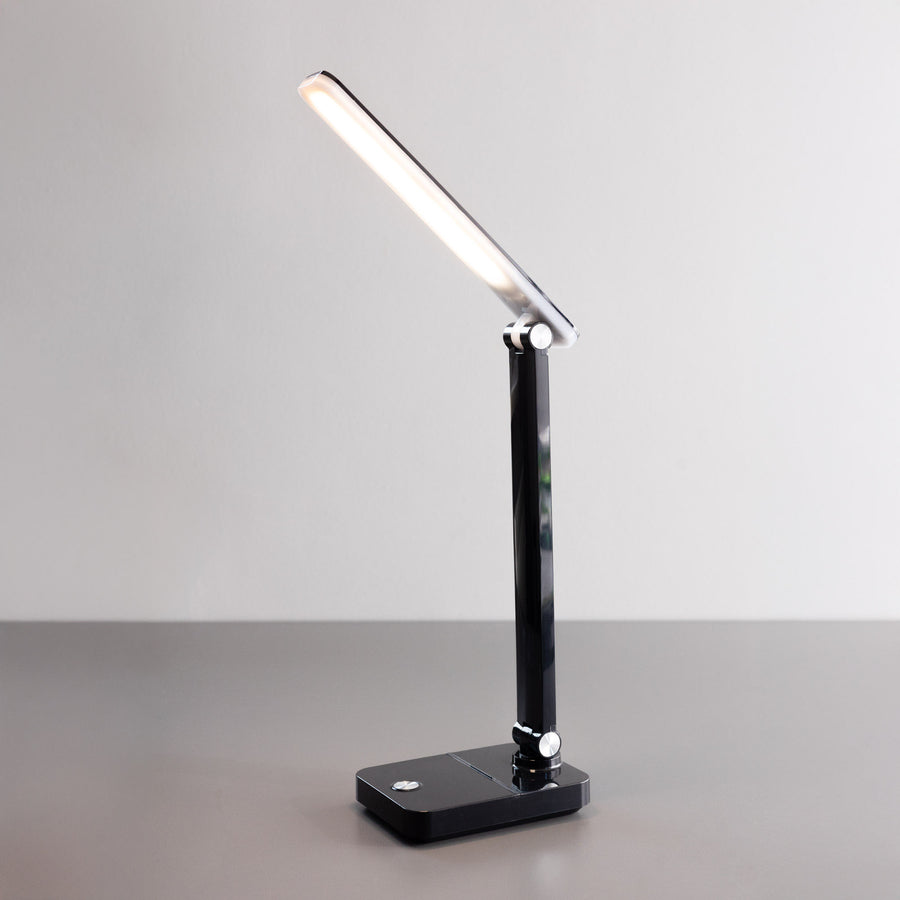 Vue de trois-quarts d'une lampe de bureau noire allumée, orientée vers le haut.