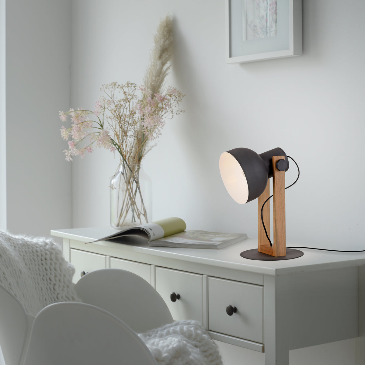 Lampe posée sur une commode blanche dans un intérieur clair avec vase et livre.