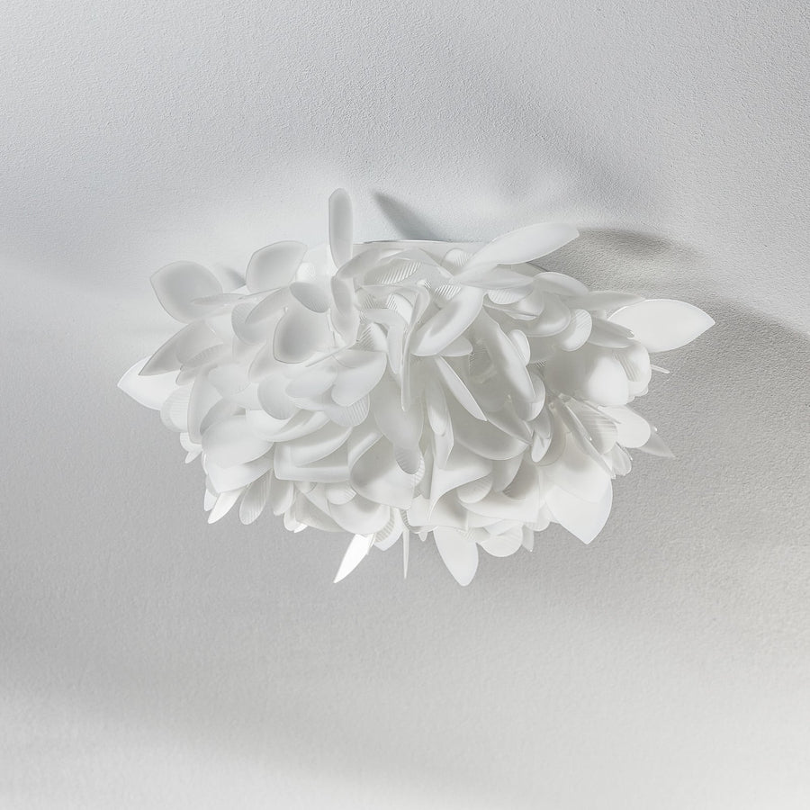 Vue de face de l'applique blanche aux pétales superposés, fixée sur un mur clair.