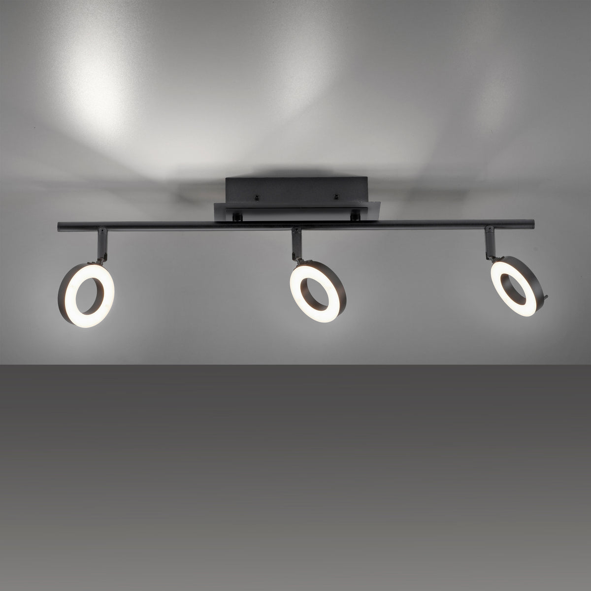 Plafonnier noir installé au plafond, trois anneaux LED diffusant une lumière chaude