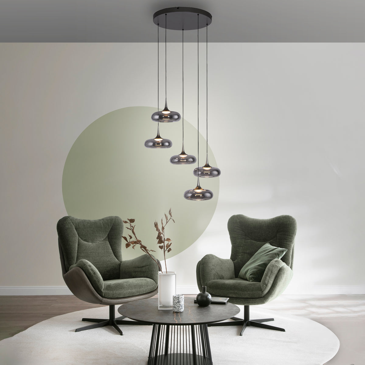 Mise en ambiance dans un salon, deux fauteuils verts et table basse sous la suspension.