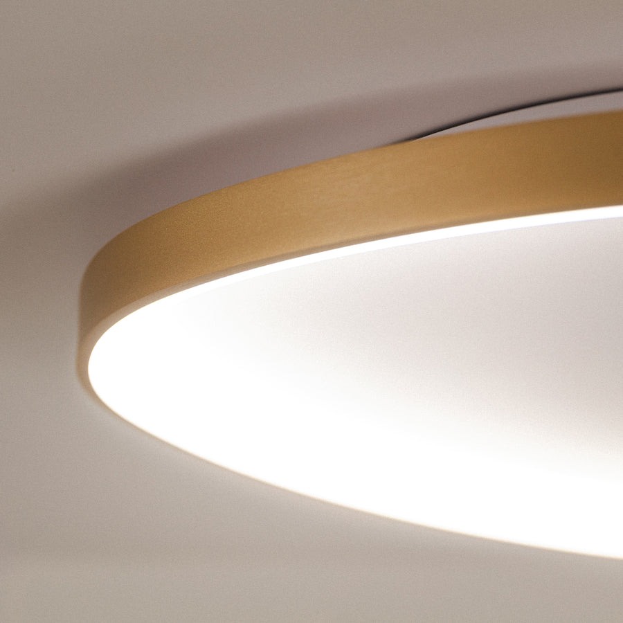 Détail du cerclage doré brossé et de la lumière blanche allumée sous le plafond.