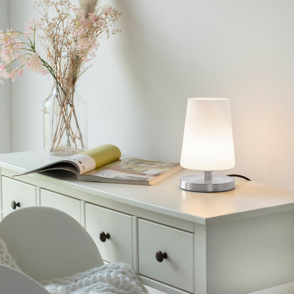 Mise en ambiance sur une commode blanche, lampe allumée près d'un magazine ouvert