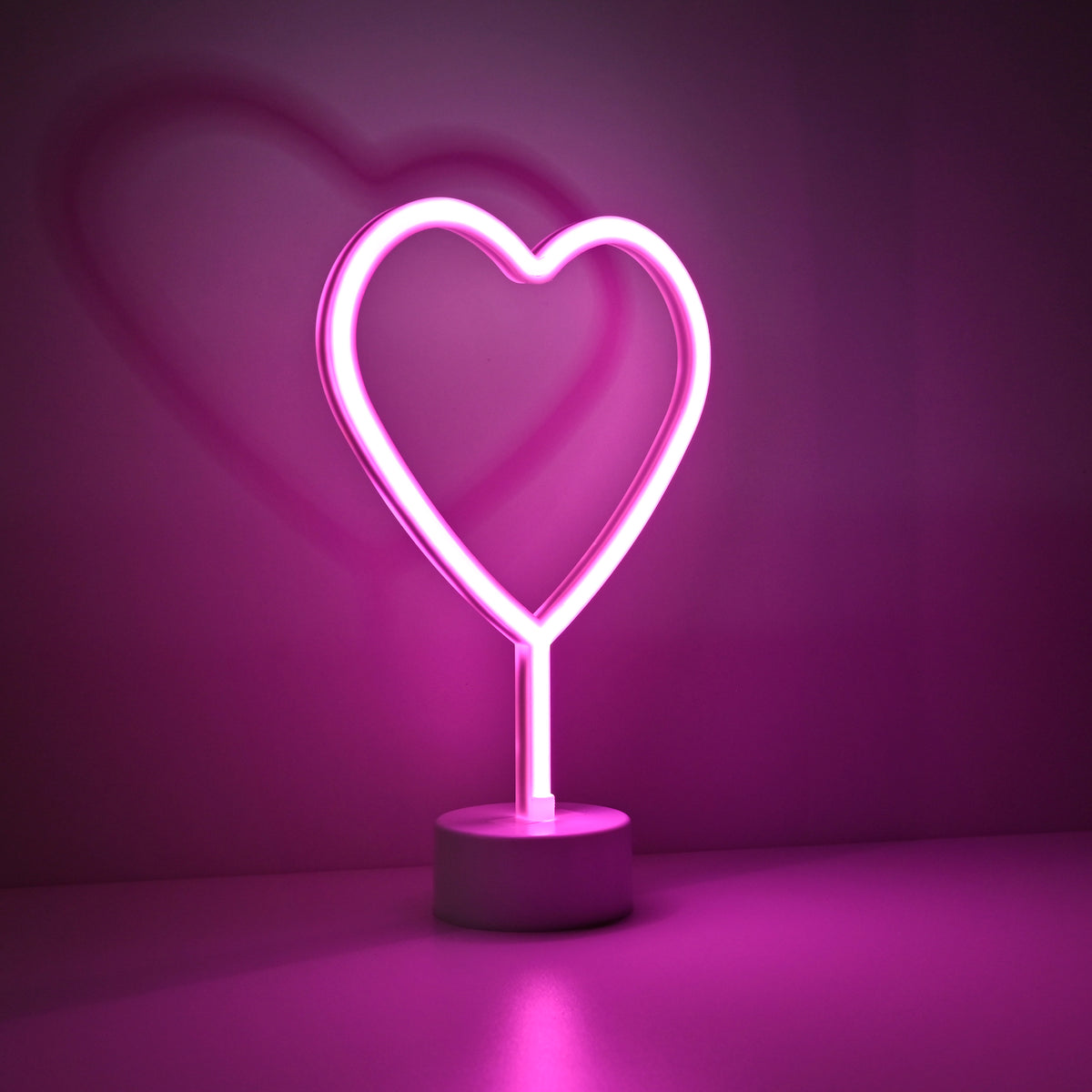 Lampe cœur rose lumineuse sur fond violet, halo rose, vue de face.