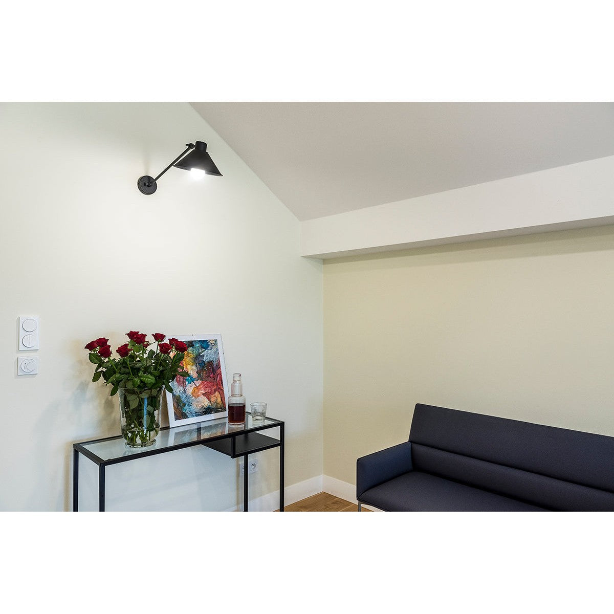 Mise en ambiance de l’applique noire fixée au mur au-dessus d’un meuble et d’un canapé.