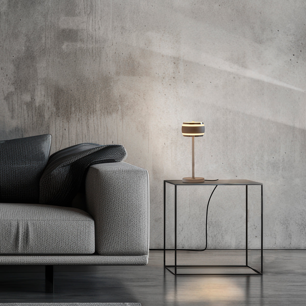 Mise en ambiance dans un salon béton, lampe posée sur table basse près du canapé