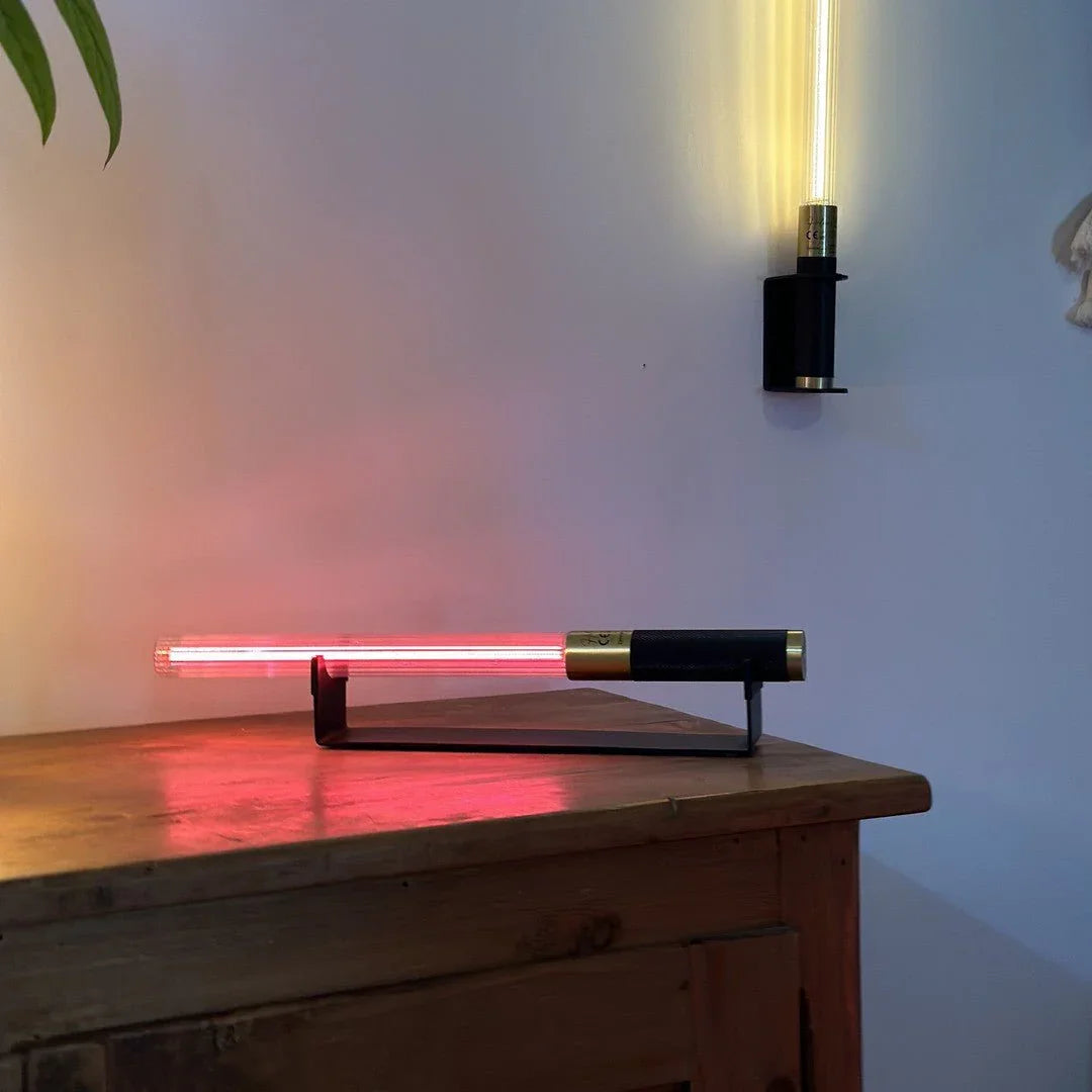 Lampe tube allumée en rouge sur commode en bois, seconde fixée au mur