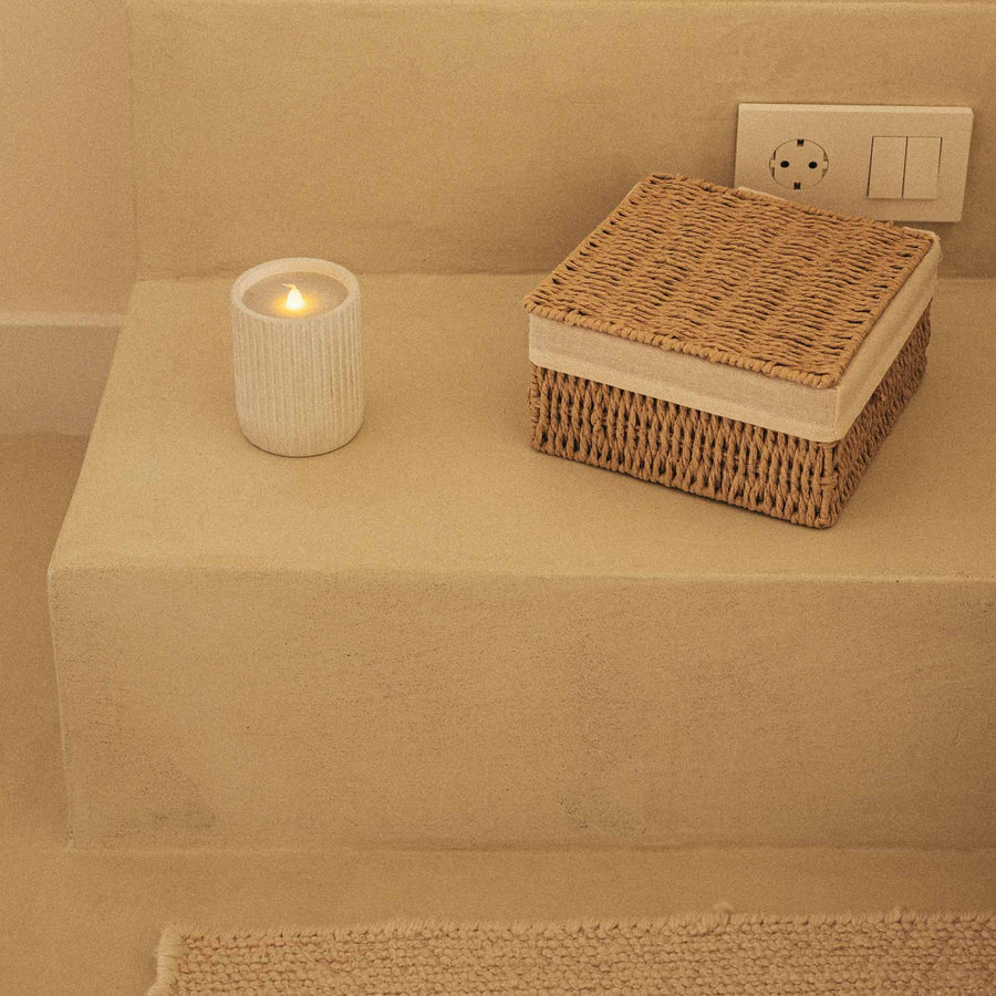 Lampe bougie allumée posée sur une marche en béton beige, près d'un panier tressé.