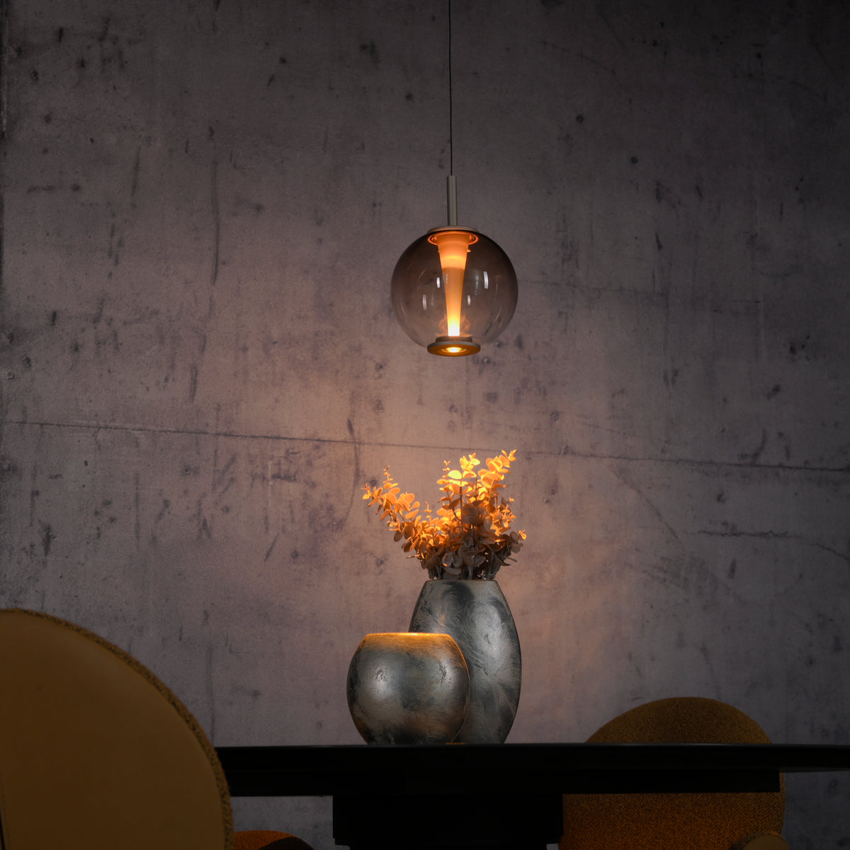 Détail en ambiance chaude, suspension éclairant un vase et des fleurs séchées.