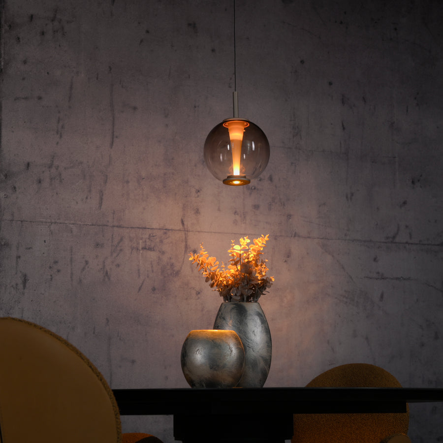 Détail en ambiance chaude, suspension éclairant un vase et des fleurs séchées.
