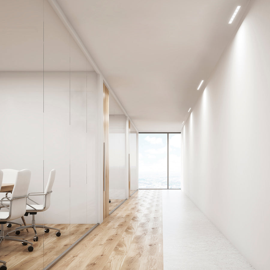 Plusieurs luminaires encastrés alignés au plafond d'un couloir de bureau.
