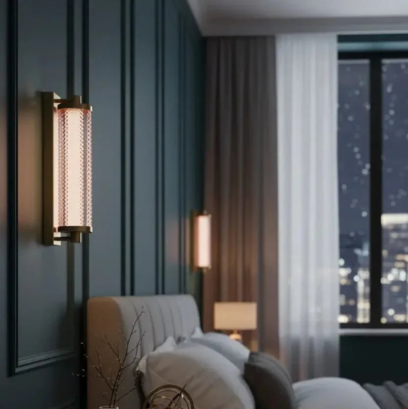 Applique cylindrique dorée fixée près d'un lit, ambiance chambre le soir avec vue urbaine