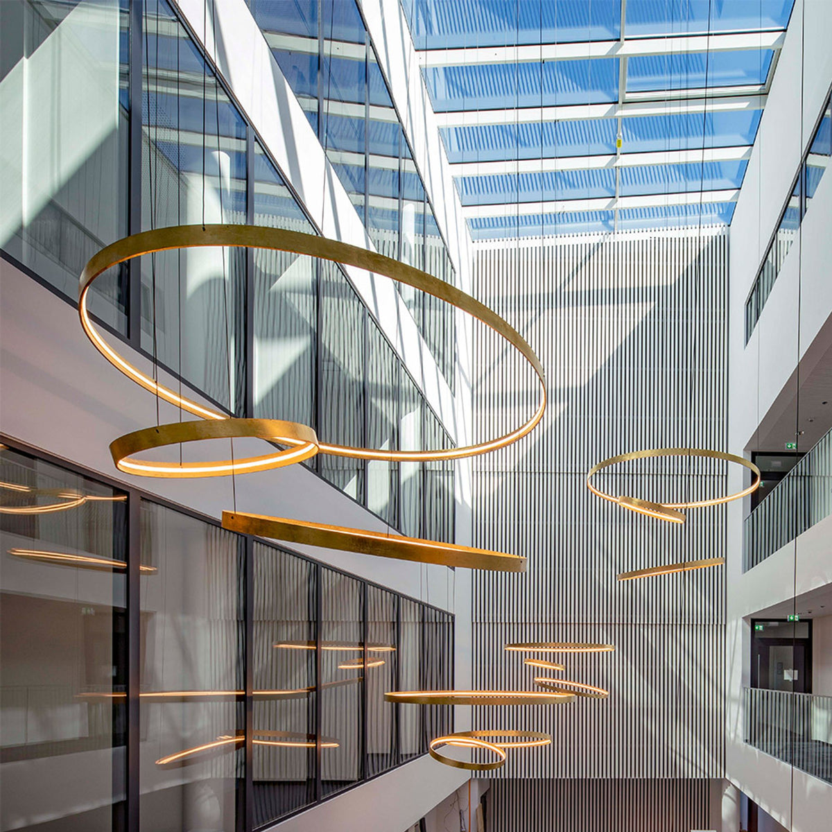 Grands cercles dorés disposés en spirale dans un atrium vitré baigné de lumière