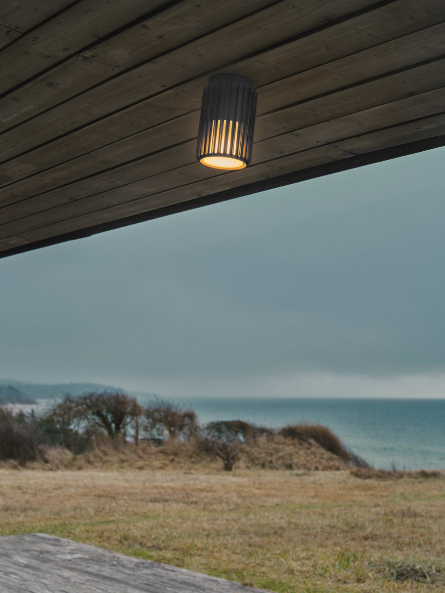 Plafonnier allumé sous une pergola en bois face à la mer, ambiance extérieure