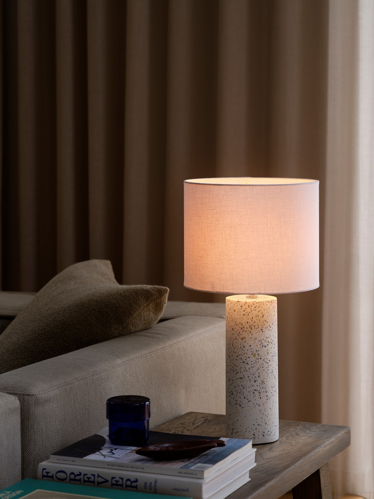 Lampe allumée posée sur table d'appoint près d'un canapé, ambiance chaleureuse et rideaux