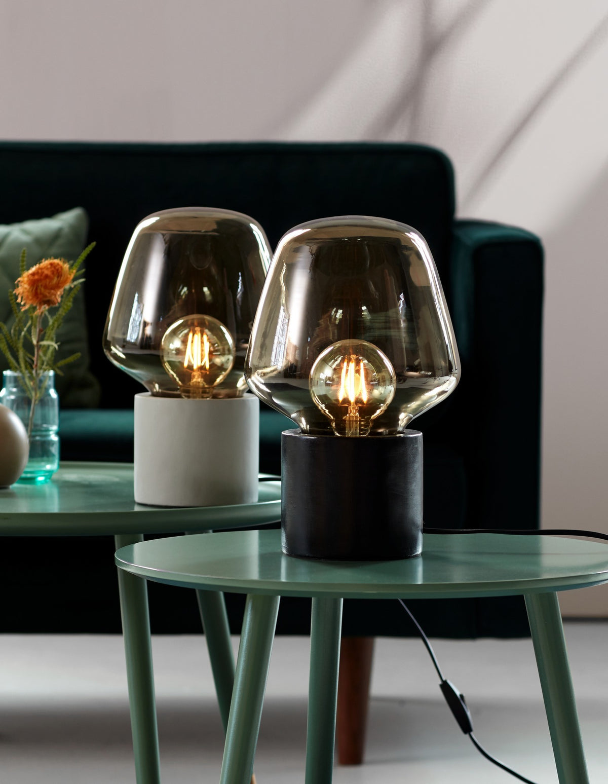 Deux exemplaires du luminaire, socles blanc et noir, posés sur tables basses vertes.