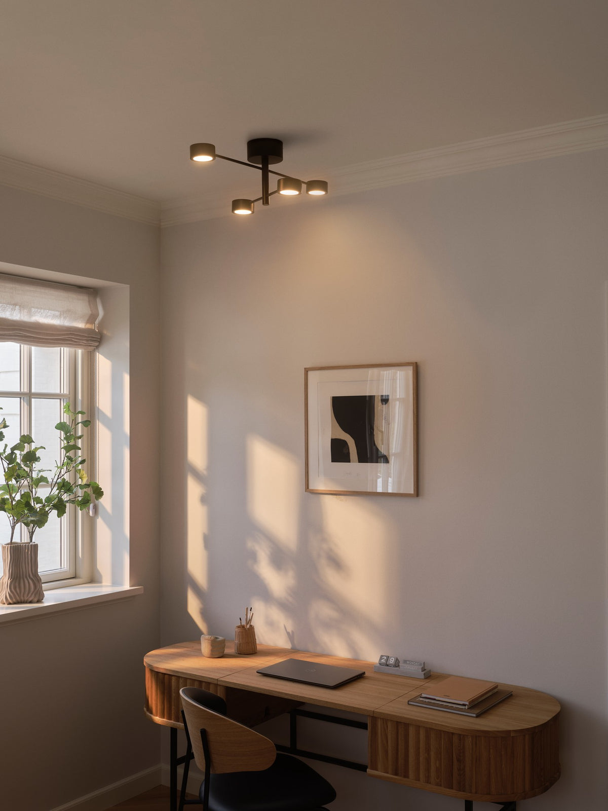 Mise en ambiance du plafonnier allumé dans un bureau moderne, au-dessus d'un bureau en bois.