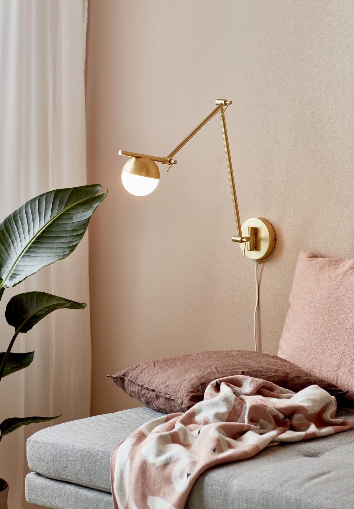 Mise en ambiance chambre avec applique murale allumée au-dessus d'un lit et coussins.