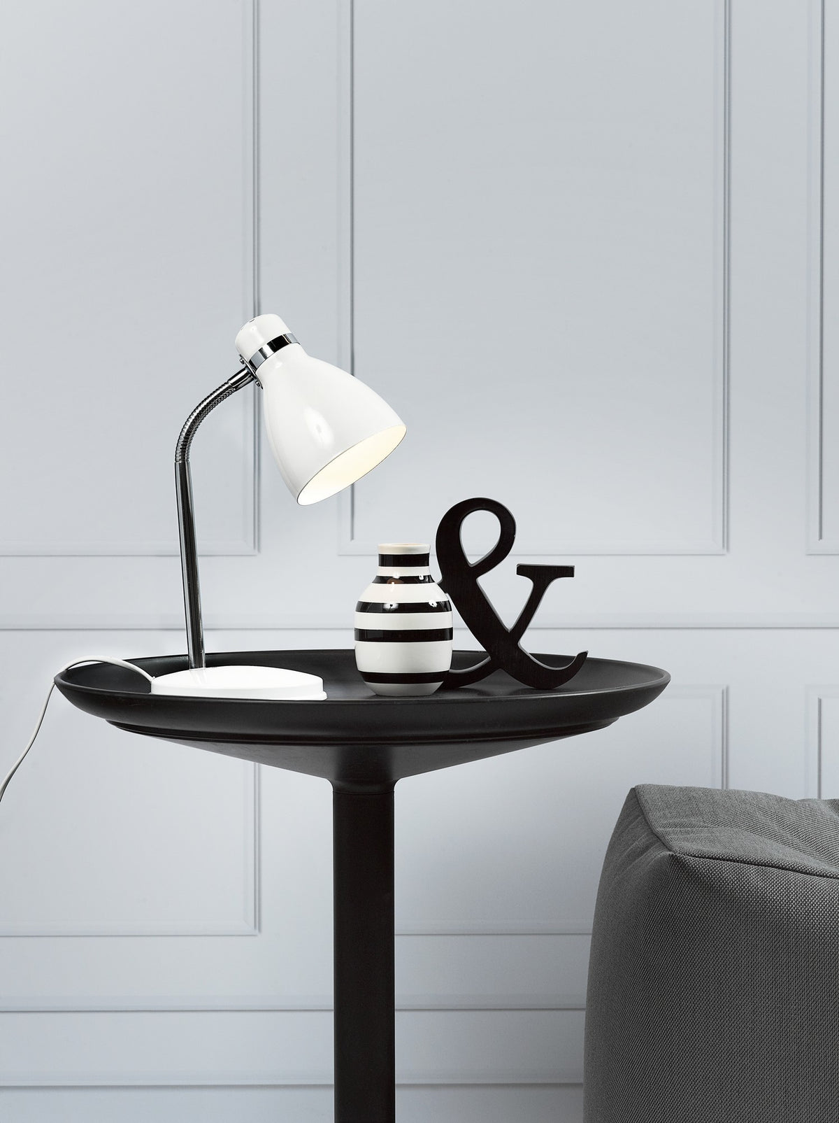 Lampe blanche posée sur table noire, vase rayé et lettre & en déco.