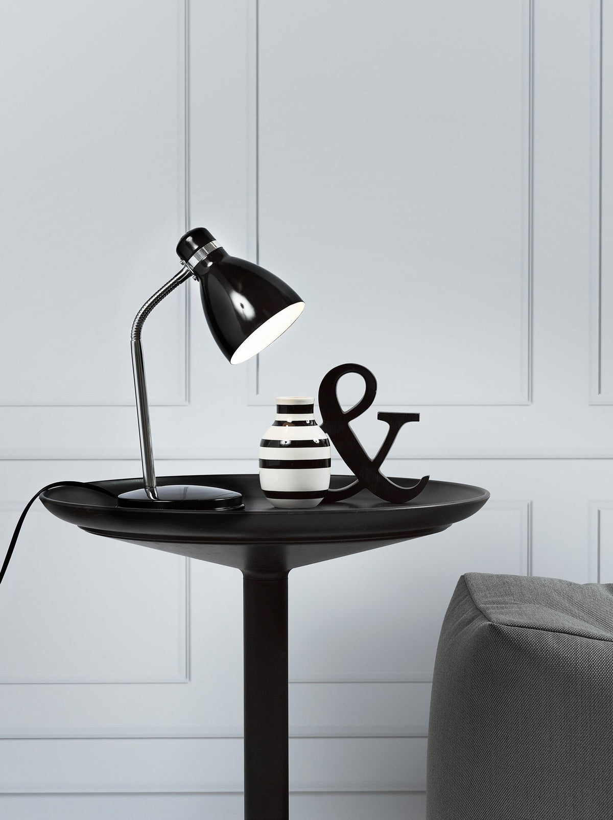 Lampe noire posée sur table noire, vase rayé et lettre & en déco.