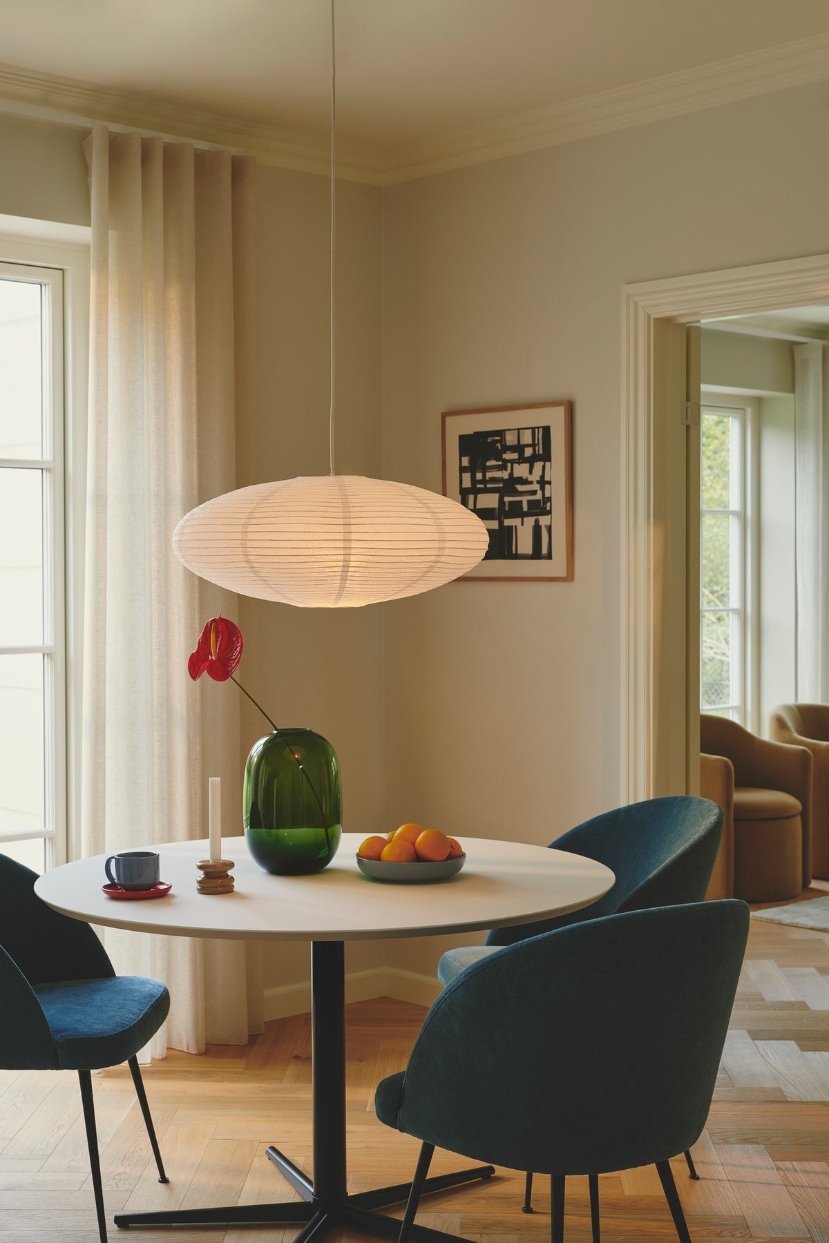 Suspension ovale en papier plissé allumée, suspendue au-dessus d'une table à manger.