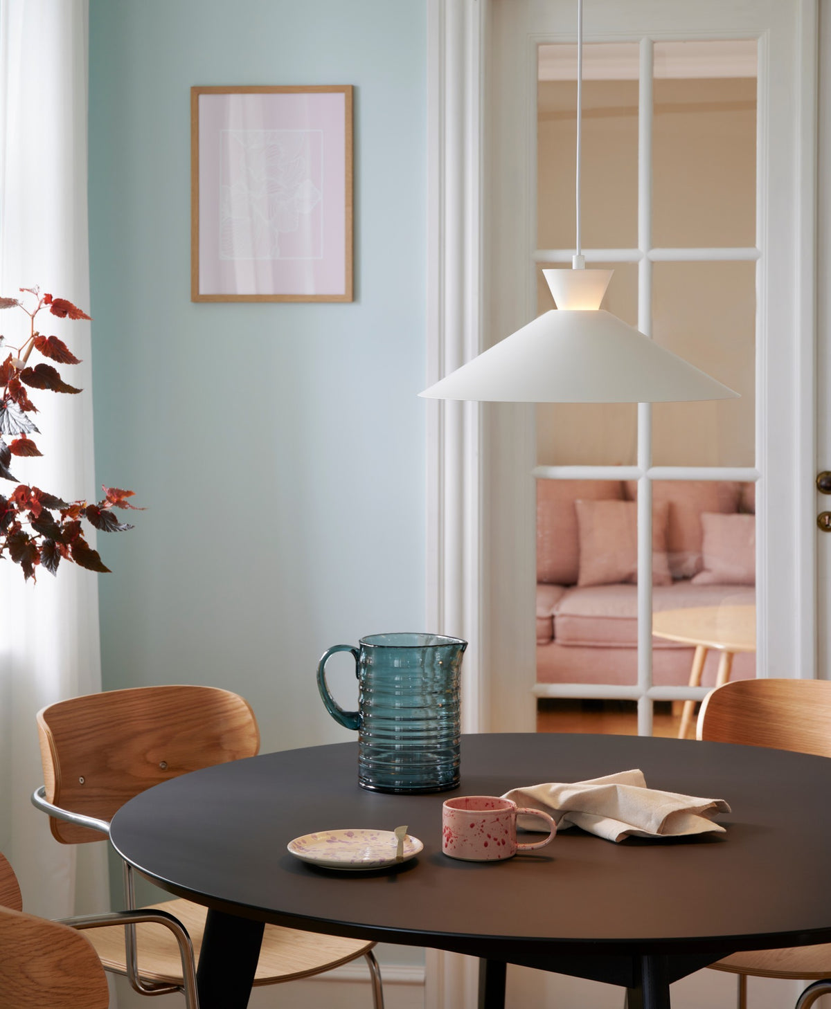 Suspension blanche allumée au-dessus d'une table ronde noire avec pichet bleu.