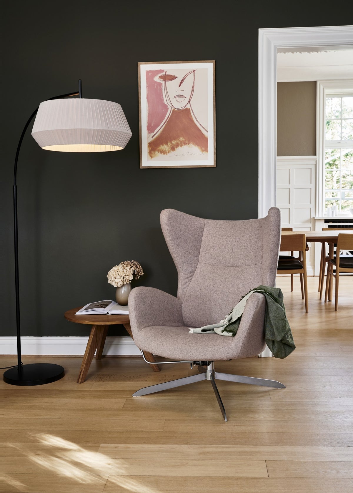 Mise en ambiance salon sombre, lampadaire près d'un fauteuil, table et tableau.