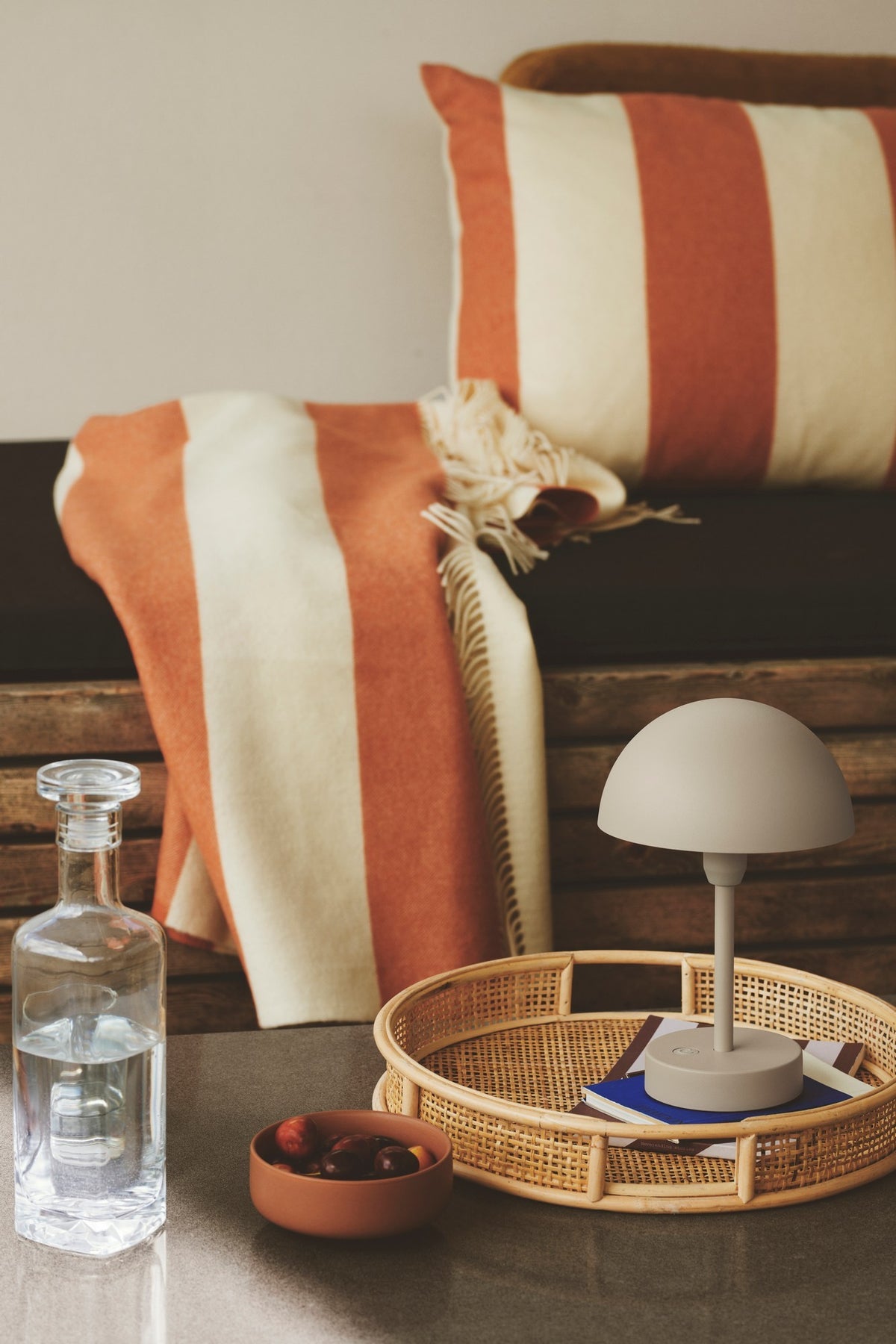 Lampe posée dans un plateau en cannage, ambiance intérieure chaleureuse avec plaid rayé.