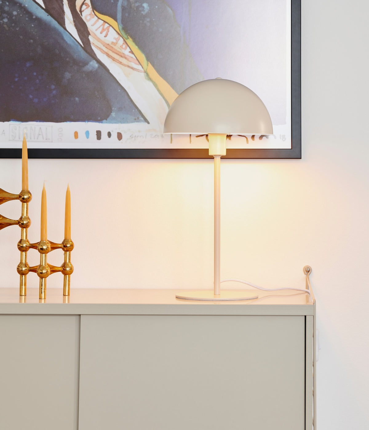Mise en ambiance sur un meuble, lampe allumée près d'un tableau et de bougeoirs dorés