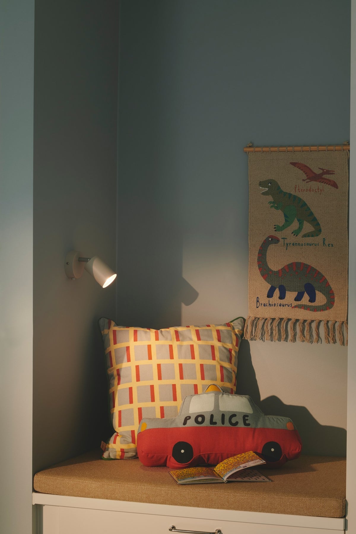 Mise en ambiance dans une chambre d'enfant, applique allumée au-dessus d'un coussin.