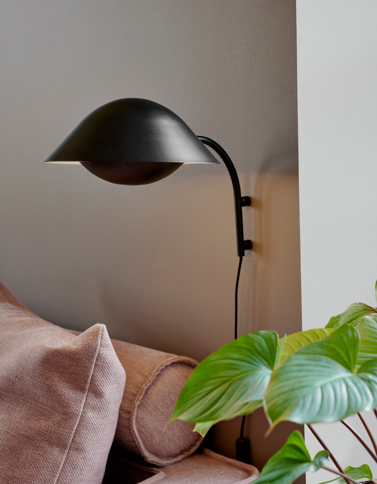 Applique murale noire installée sur un mur beige au-dessus d'un canapé rose.