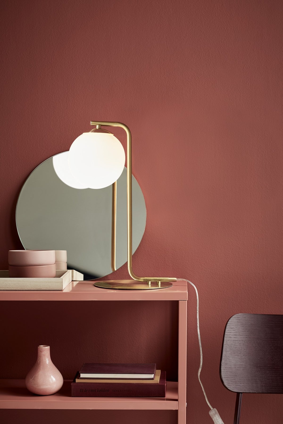 Lampe allumée posée sur une console rose devant un miroir rond