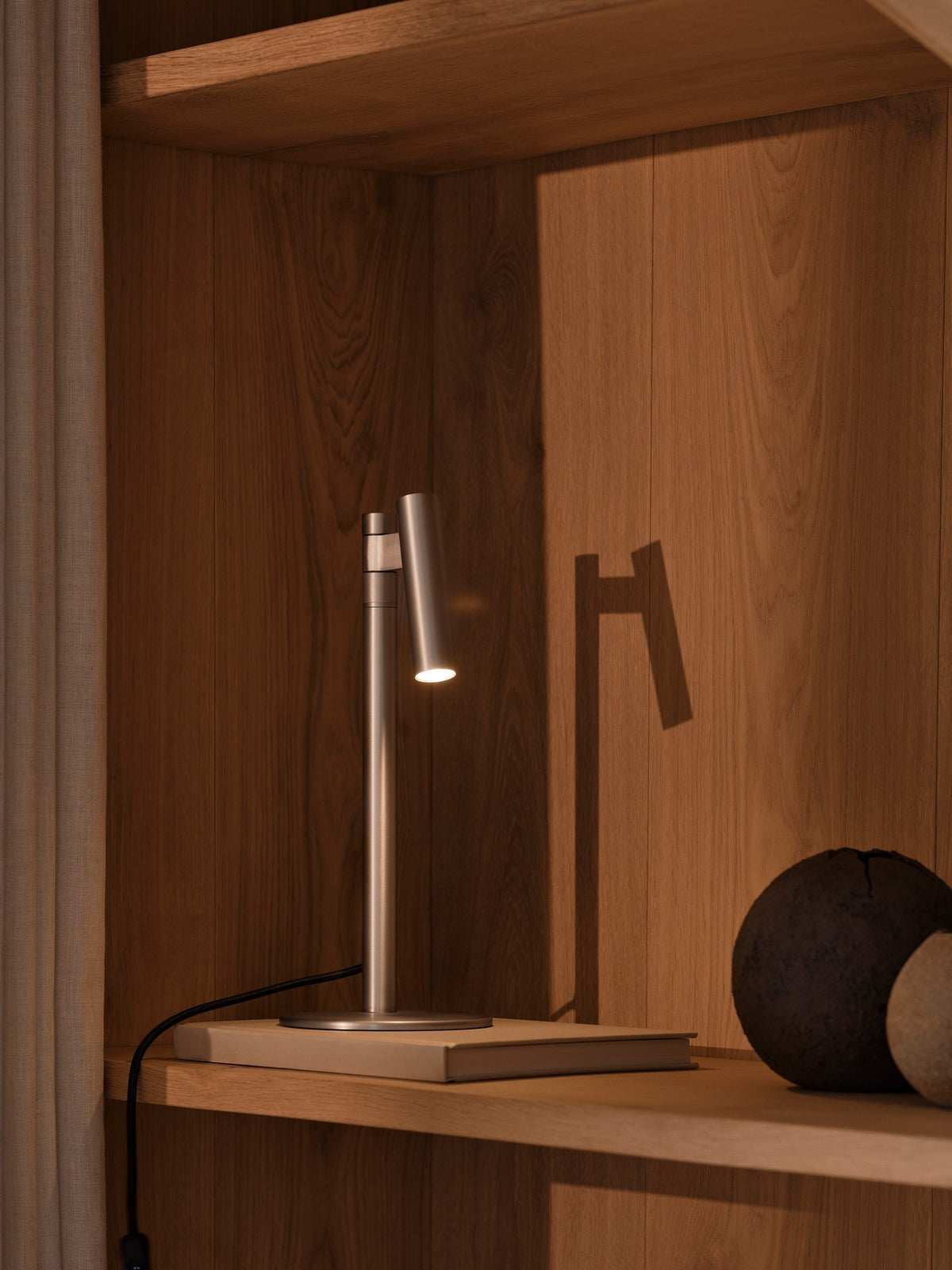 Mise en ambiance sur une étagère en bois avec livres et lumière chaude dirigée.