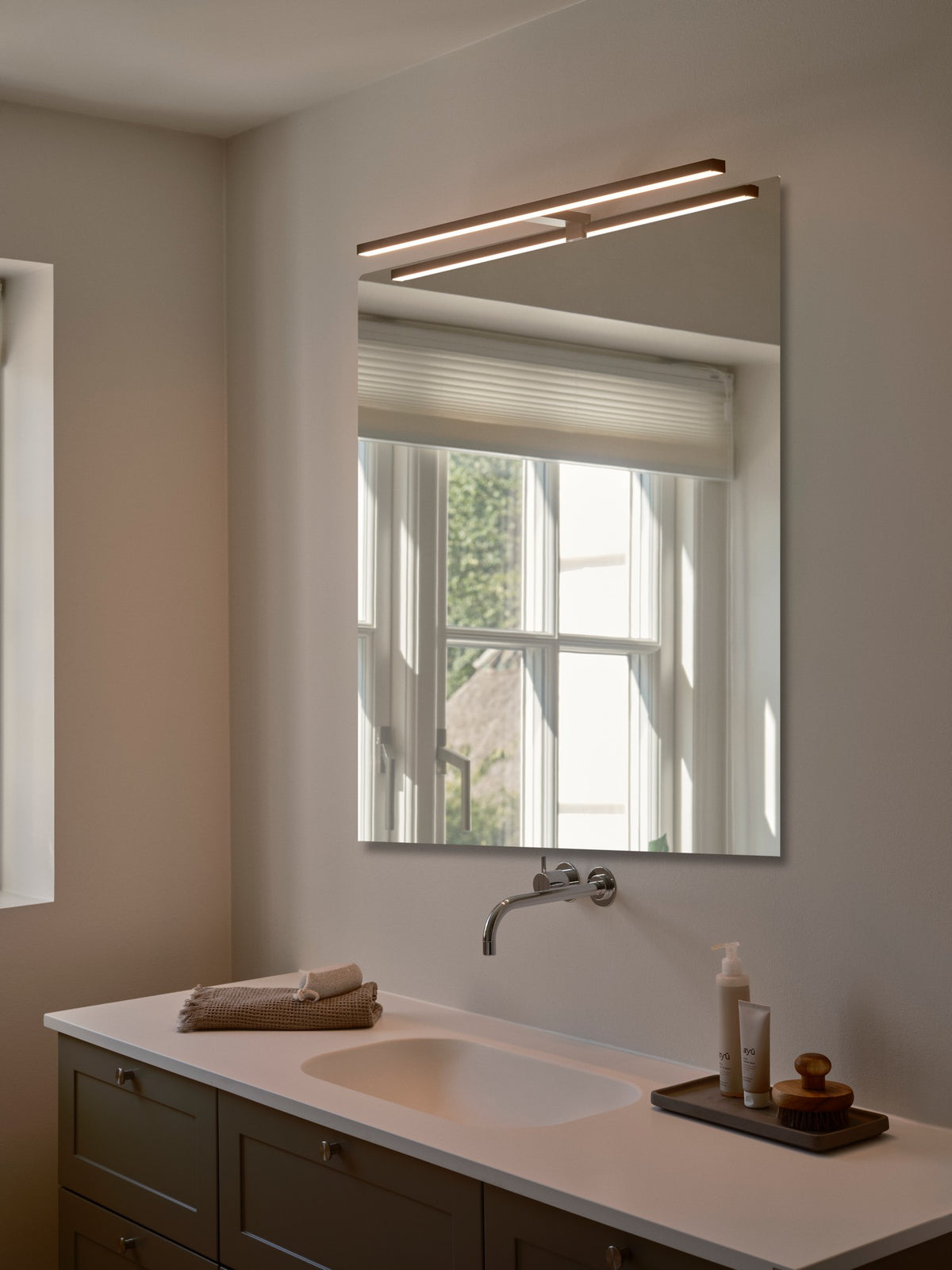 Mise en ambiance salle de bain, applique murale noire éclairant un miroir et un lavabo.