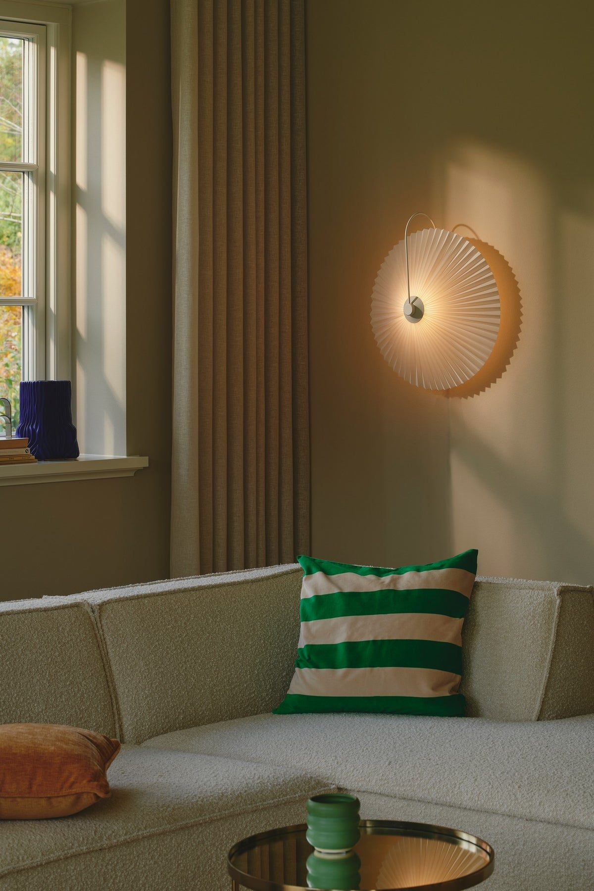 Mise en ambiance dans un salon : applique allumée au-dessus d'un canapé beige