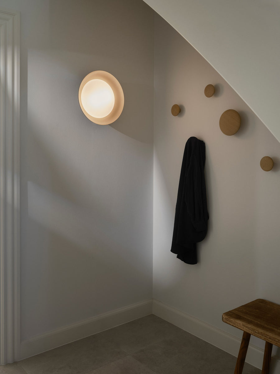 Luminaire allumé au plafond dans un couloir avec patères murales et tabouret.