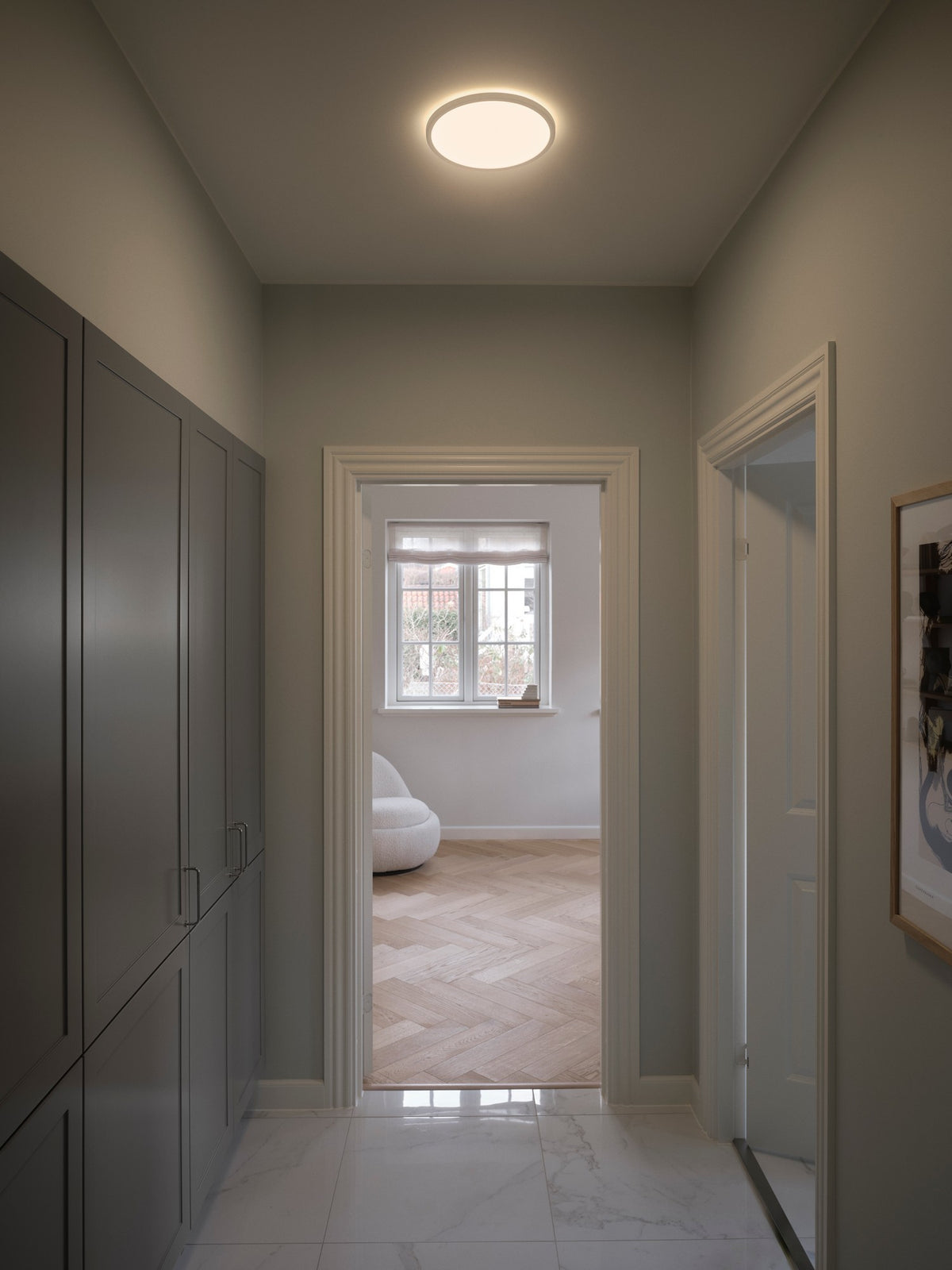 Plafonnier LED rond allumé dans un couloir contemporain aux murs gris, mise en ambiance.