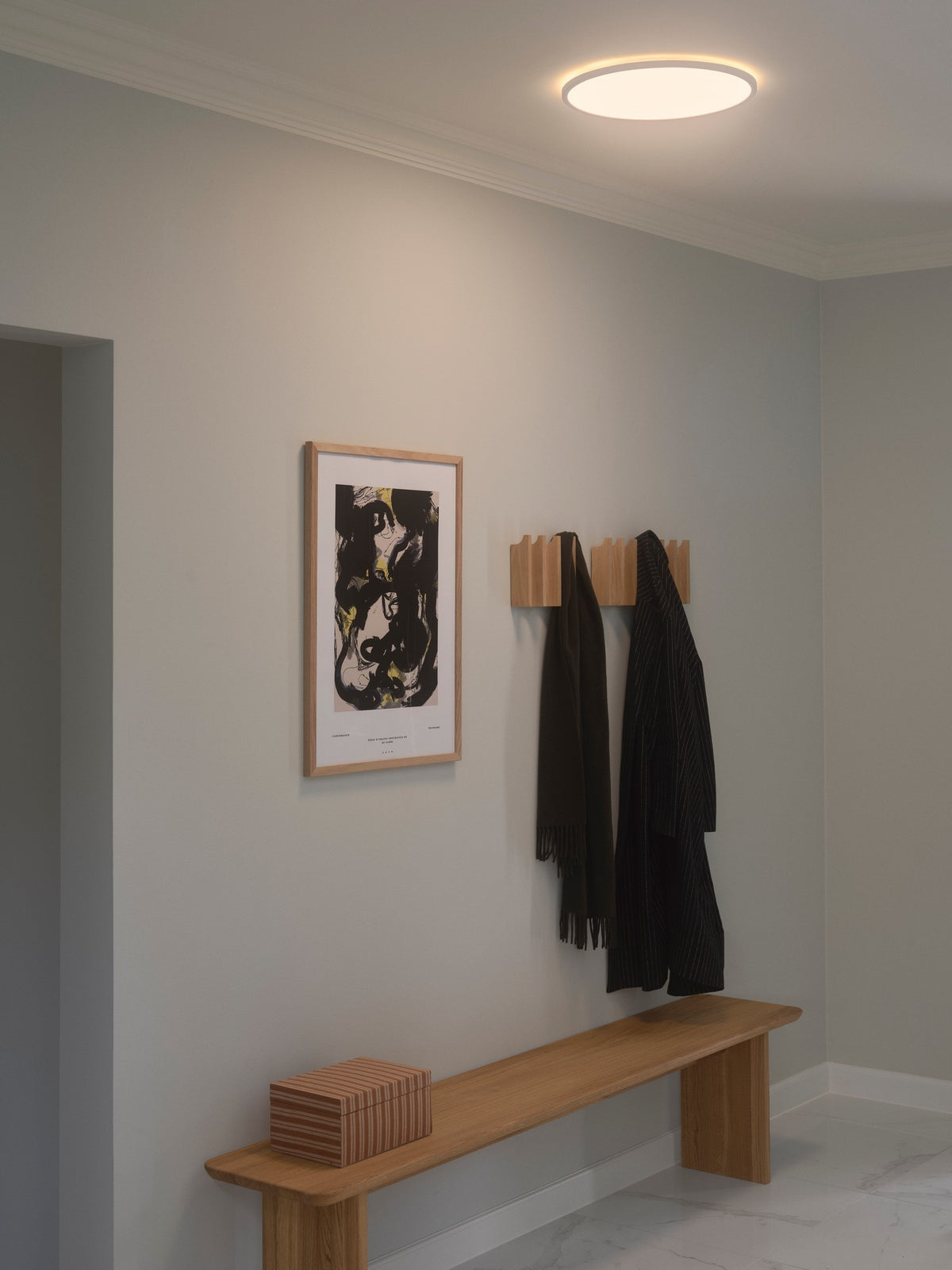 Mise en ambiance dans une entrée moderne, plafonnier allumé au-dessus du banc