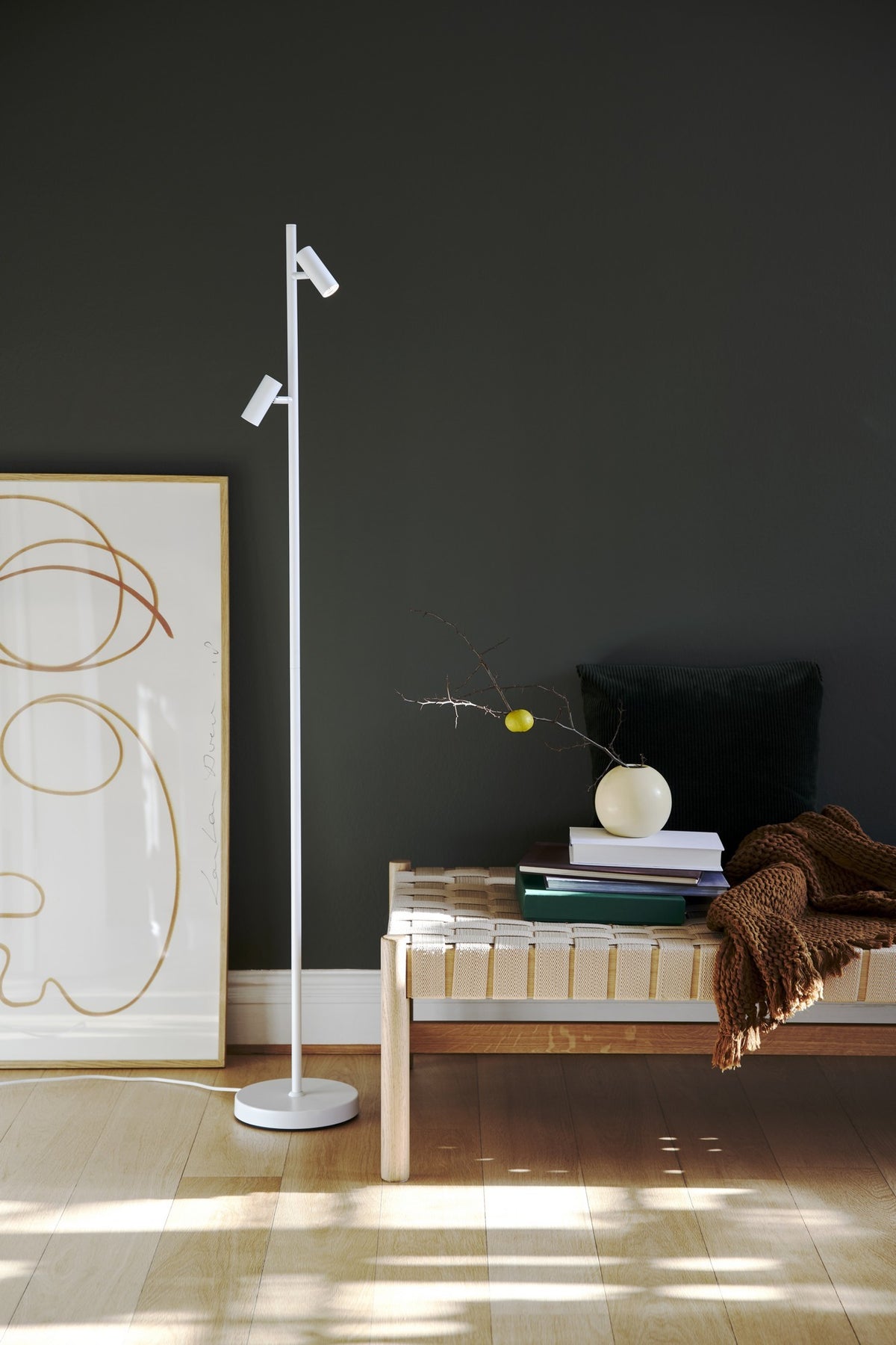 Mise en ambiance : lampadaire blanc allumé dans un salon sombre près d'un banc.