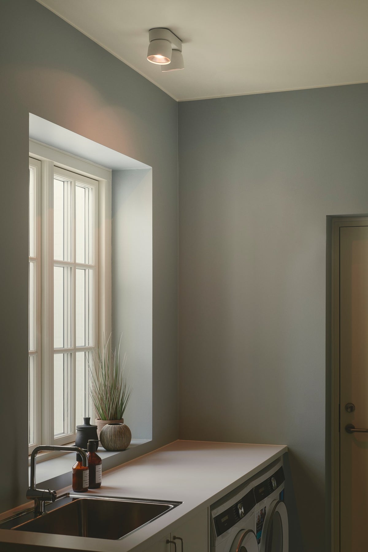 Mise en ambiance : plafonnier blanc fixé au plafond d'une buanderie au-dessus de l'évier