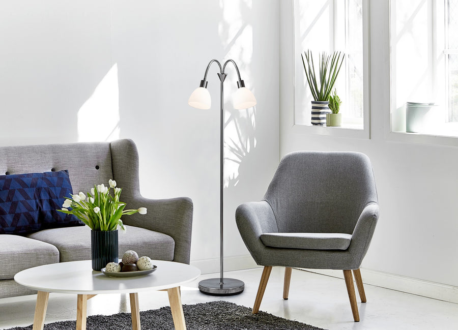 Lampadaire double allumé dans un salon contemporain, canapé gris, table basse blanche et plante.