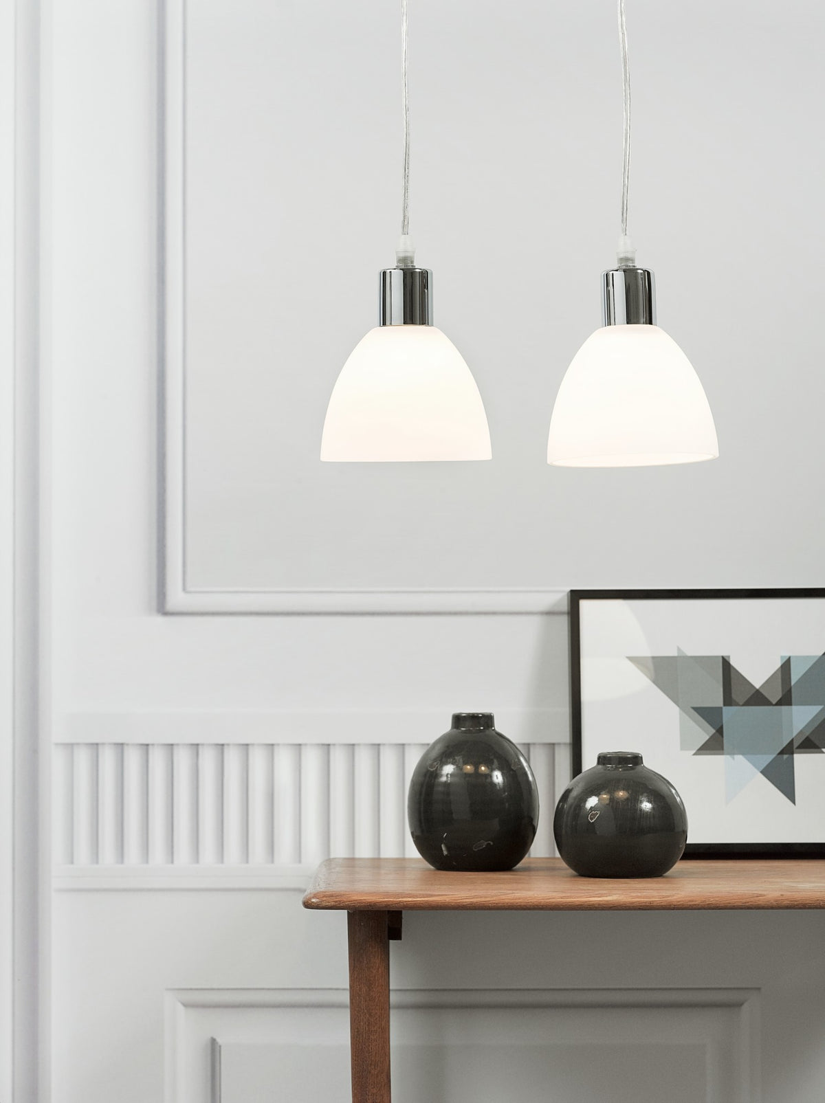Suspensions blanches devant un mur clair, décor minimaliste avec vases sombres sur console en bois.