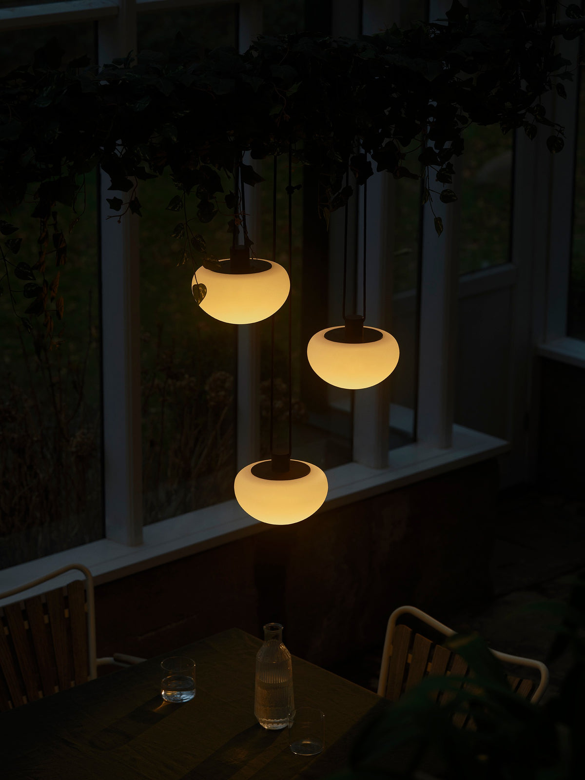 Mise en ambiance nocturne, trois suspensions blanches allumées au-dessus d'une table en bois