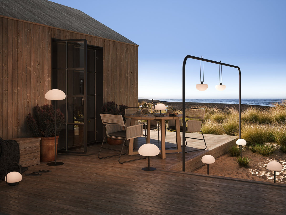 Scène extérieure avec plusieurs luminaires nomades suspendus, posés au sol ou sur table.
