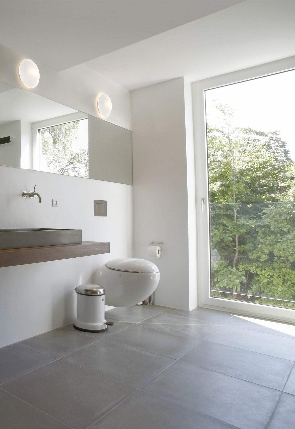 Vue d'ambiance d'une salle de bain avec deux luminaires ronds blancs allumés près du miroir.