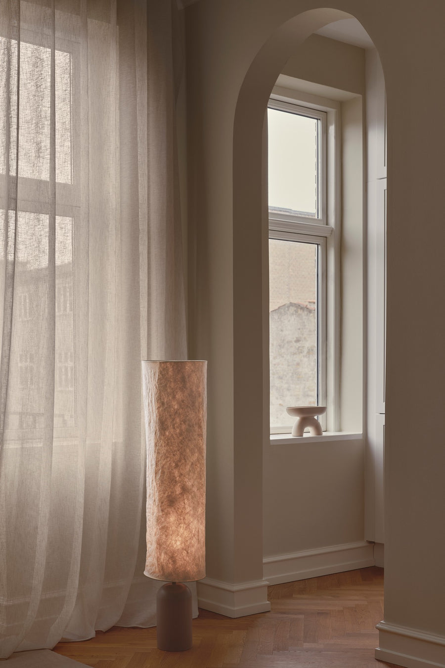 Lampadaire dans un intérieur avec rideaux transparents et fenêtre cintrée.