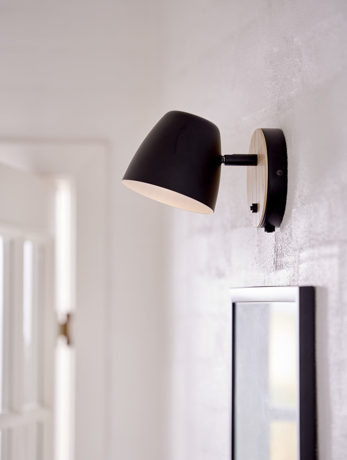Mise en ambiance de l'applique allumée sur un mur blanc près d'un miroir