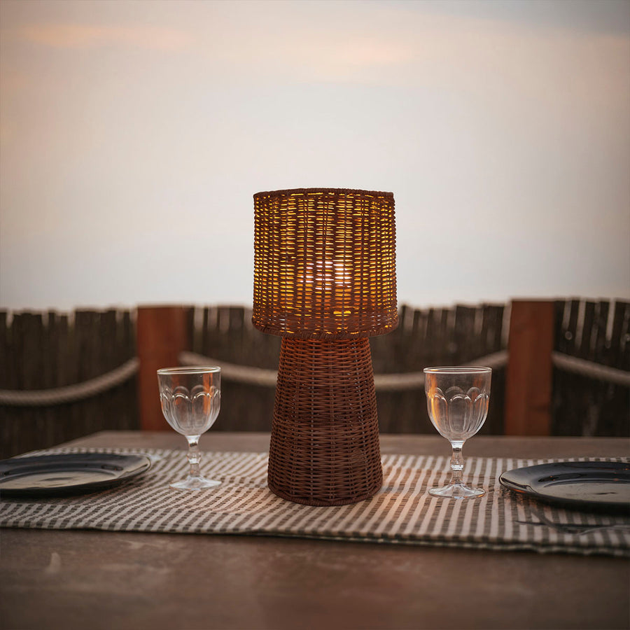 Lampe posée sur une table dressée, verres et assiettes au coucher du soleil